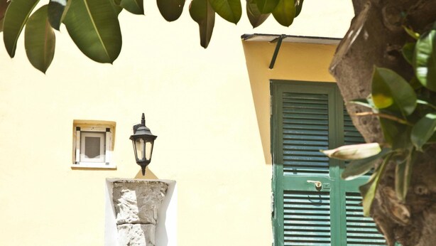 Fachada de edifício com uma pequena janela, um poste de luz e uma porta com persiana verde.