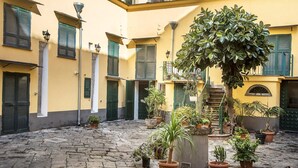 Une cour avec des murs jaunes, des volets verts et des plantes en pot.