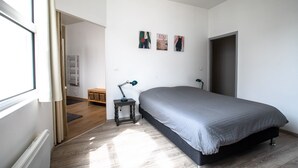 A bedroom with a large bed, a small bedside table with a lamp, a radiator, and a wardrobe. - Le Loft Horloger (Besançon)