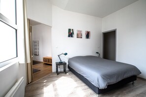 A bedroom with a large bed, a small bedside table with a lamp, a radiator, and a wardrobe. - Le Loft Horloger (Besançon)