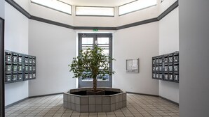 A lobby with a central planter, a door with an exit sign, and storage lockers on either side. - Le Loft Horloger (Besançon)
