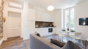 A modern kitchen with white cabinets, a dining area with a table set for two, and a grey sofa with cushions. - Co-c520-vmon4a1 - Amazing Cernobbio (Cernobbio)