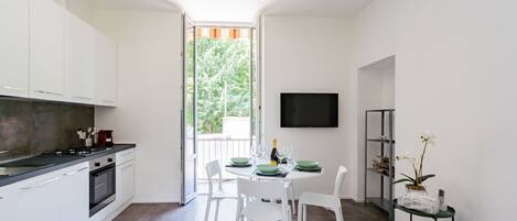 Una cocina moderna con armarios blancos, encimera negra y una zona de comedor con sillas blancas y una mesa redonda.
