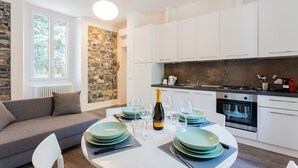 A modern kitchen with white cabinets, a stone accent wall, and a dining area set up with green plates and wine glasses. - Co-c520-vmon4a1 - Amazing Cernobbio (Cernobbio)
