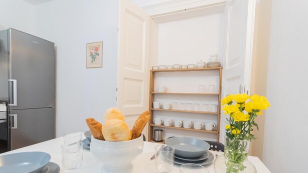 A kitchen with a refrigerator, a bowl of bread, a vase with yellow flowers, and a shelf with cups and plates. - Da Pia in Historycal Como City Centre (Como)