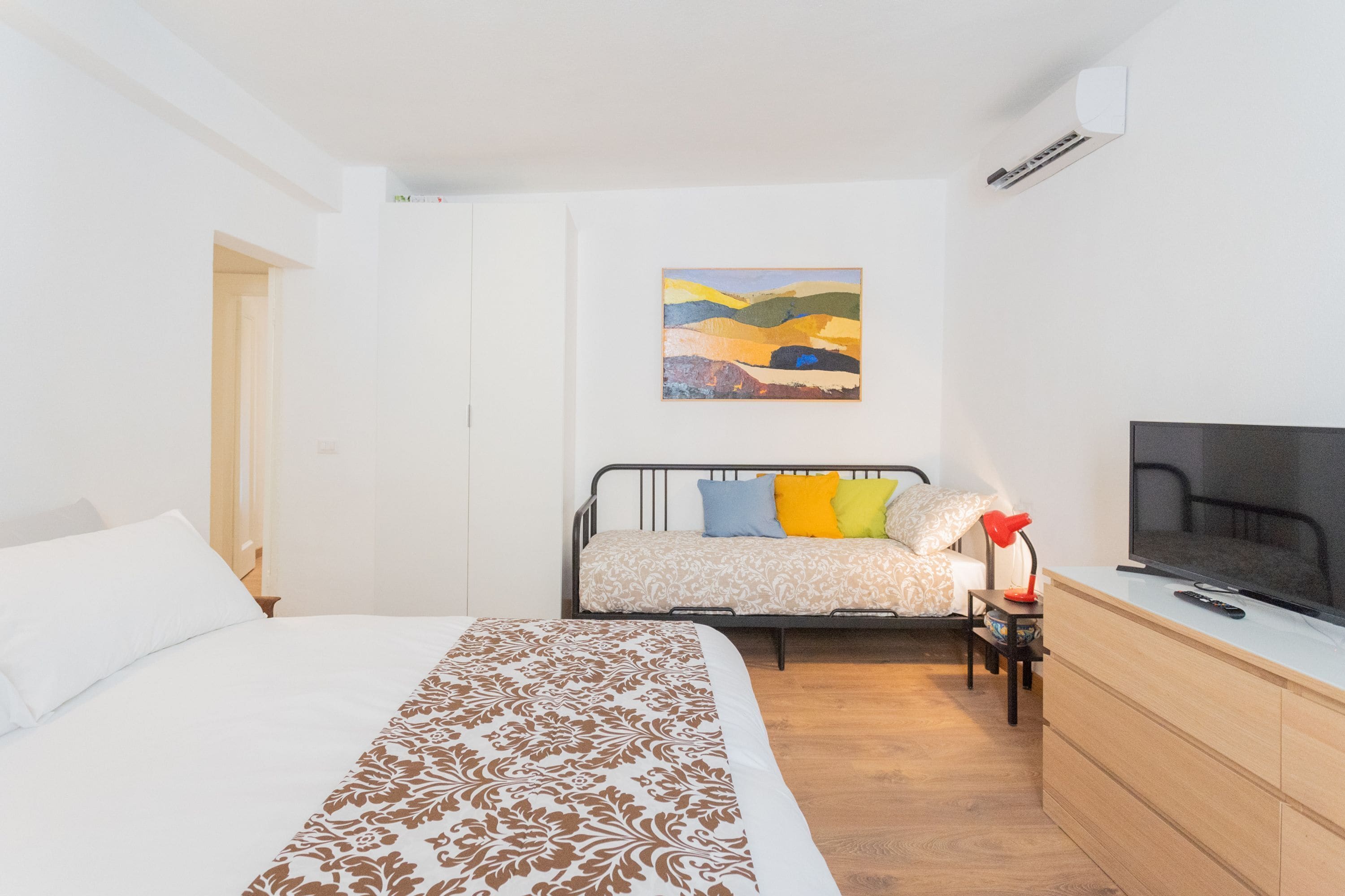 A bedroom with a bed, a TV, a dresser, and a painting on the wall.