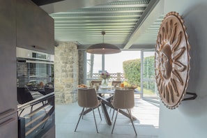 A modern kitchen with a built-in oven, a dining area with a table and chairs, and a large window offering a view of the outdoors. - Co-h679-stat6bt - Villa Sasso On Lake Como (Sala Comacina)