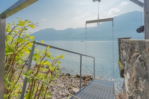 Eine Treppe führt zu einer Plattform mit Blick auf ein Gewässer, im Hintergrund Berge.