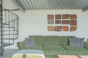 A green sofa with two pillows, a spiral staircase, and a wall with nine textured tiles.