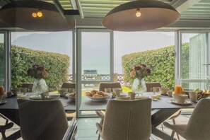 A dining table set with plates, bowls, and cups, with a view of a garden and mountains through large windows.