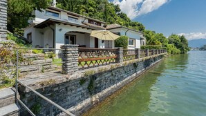 A lakeside property with a stone wall, a wooden deck, and a large umbrella. - Villa Bianca - Front Lake Pool (Sala Comacina)