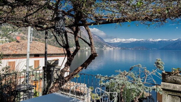 Eine Terrasse mit einem Metalltisch und -stühlen mit Blick auf einen See, im Hintergrund Berge.