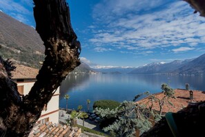Vista para o lago, com montanhas ao fundo, um edifício com telhado de azulejos e céu claro.