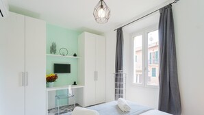 Ein Schlafzimmer mit einem Bett, einem Fernseher, einem Schreibtisch und einem Fenster mit Vorhängen.
