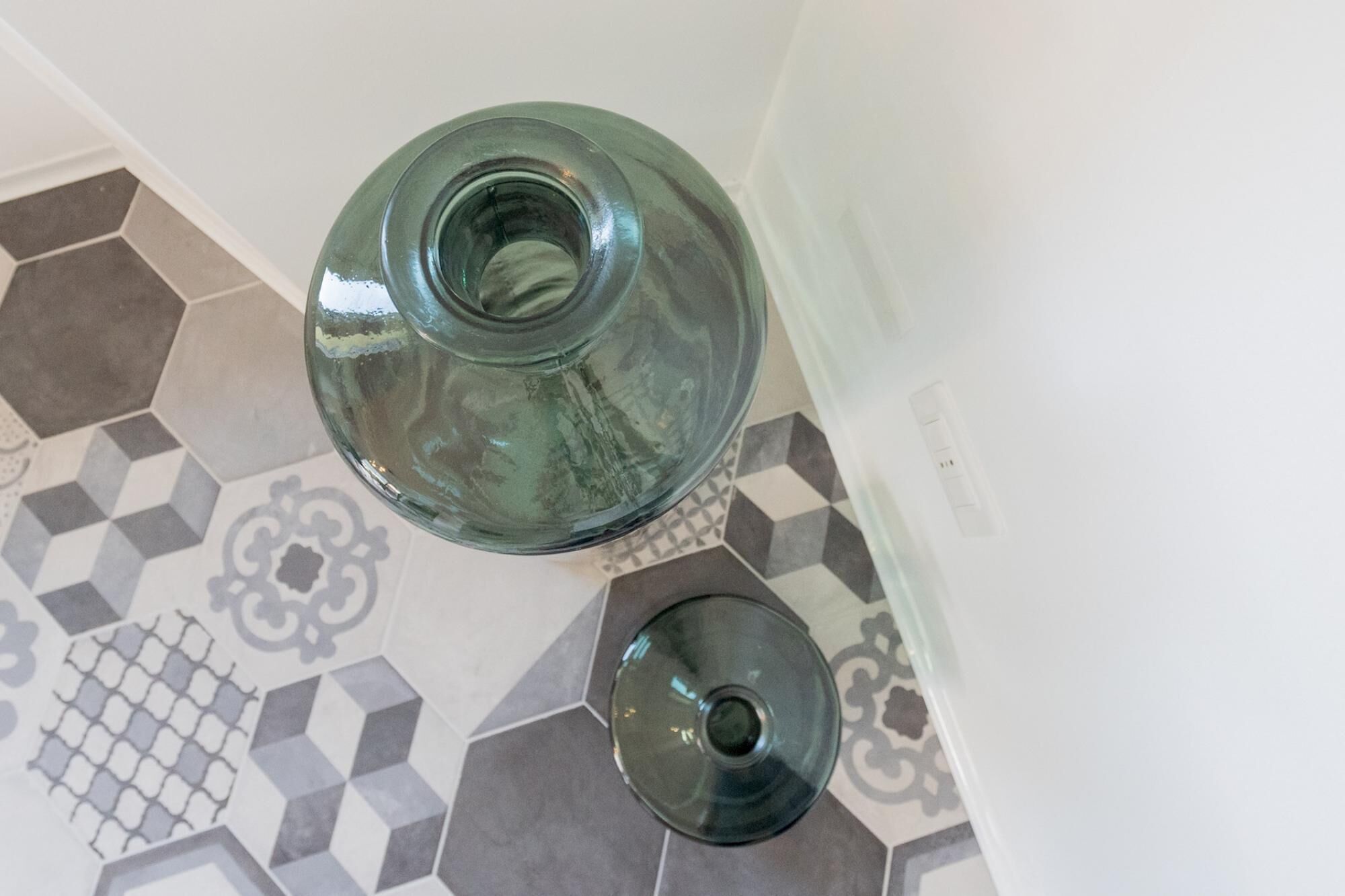 A bathroom with a glass vase and a smaller container on a tiled floor.