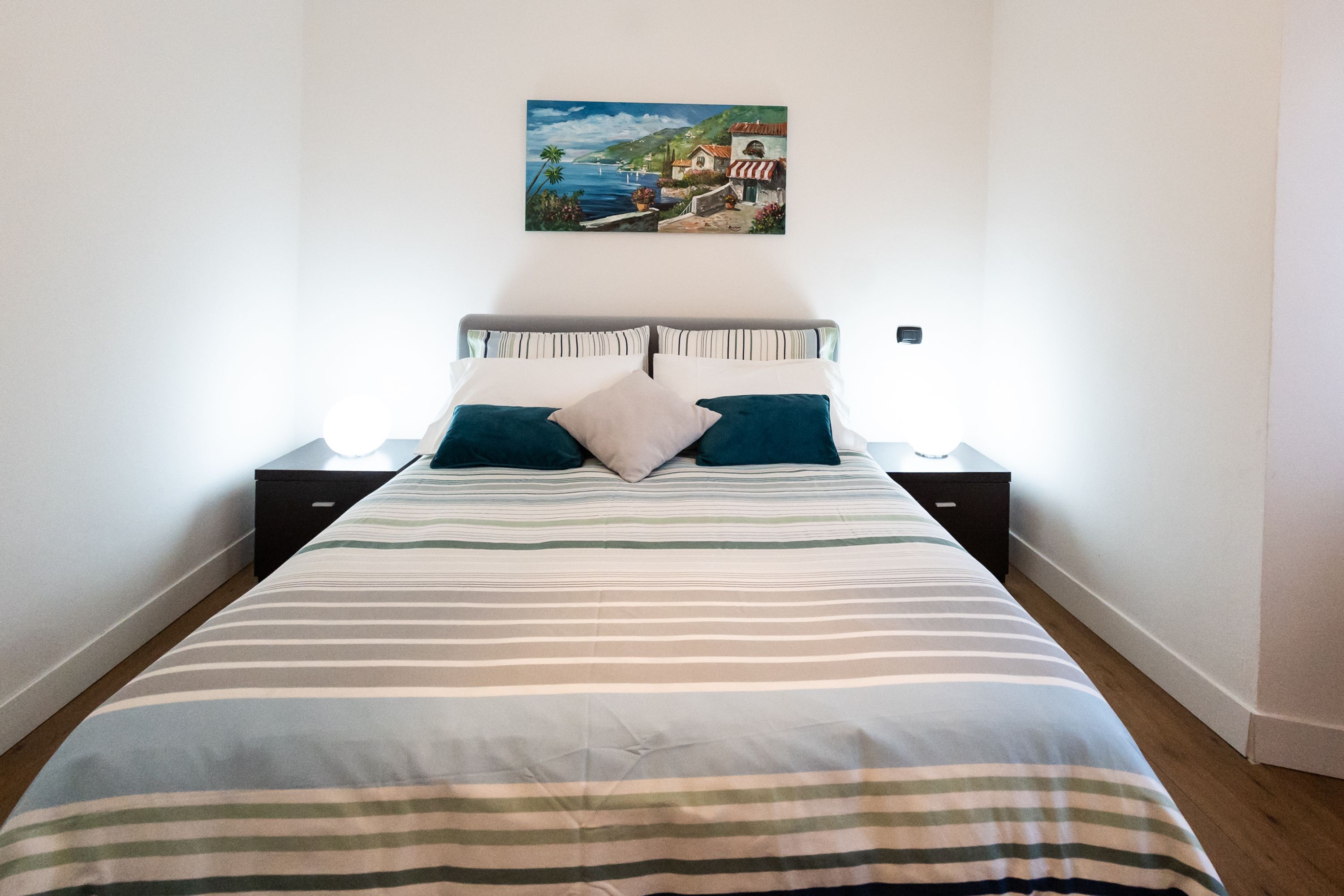 Cama bem arrumada com roupa de cama listrada, dois travesseiros e uma mesa de cabeceira com abajur.