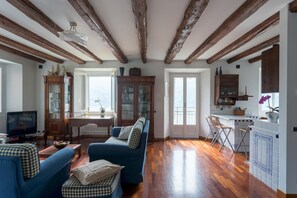 Amplia sala de estar con vigas de madera, un sofá azul, un mueble de madera y una zona de cocina con ventanal.