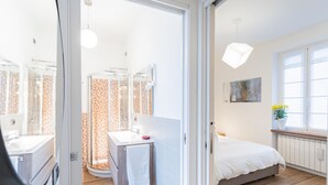 A modern bedroom with a large bed, a bedside table, a window with a view, and a bathroom with a shower and a mirror. - Co-c933-dott13a2 - Rosart House (Como)