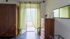 Ein Zimmer mit einem Holzschrank, einer Kommode mit Schubladen, einem Spiegel und Blick durch eine Tür mit transparenten Vorhängen.