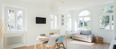 A bright, spacious room with a dining area, a sofa, and a TV mounted on the wall.