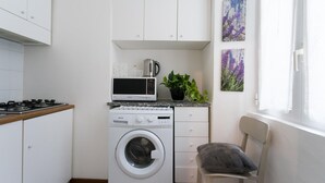 Ett kompakt kök med tvättmaskin, mikrovågsugn och en liten matplats med en stol.