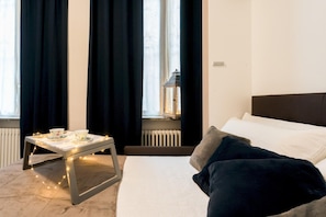 A hotel room with a bed, a bedside table with a cup and saucer, a string of lights, and a window with curtains. - Co-c933-ggar24d1 - Love Smile Apartment (Como)