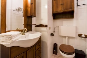 Een badkamer met een wastafel, spiegel, houten kastjes, toilet en douche.