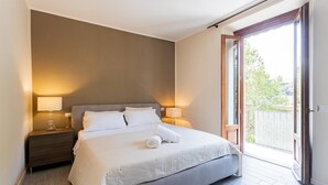 A bedroom with a bed, two bedside lamps, a nightstand, and a sliding glass door to a balcony.