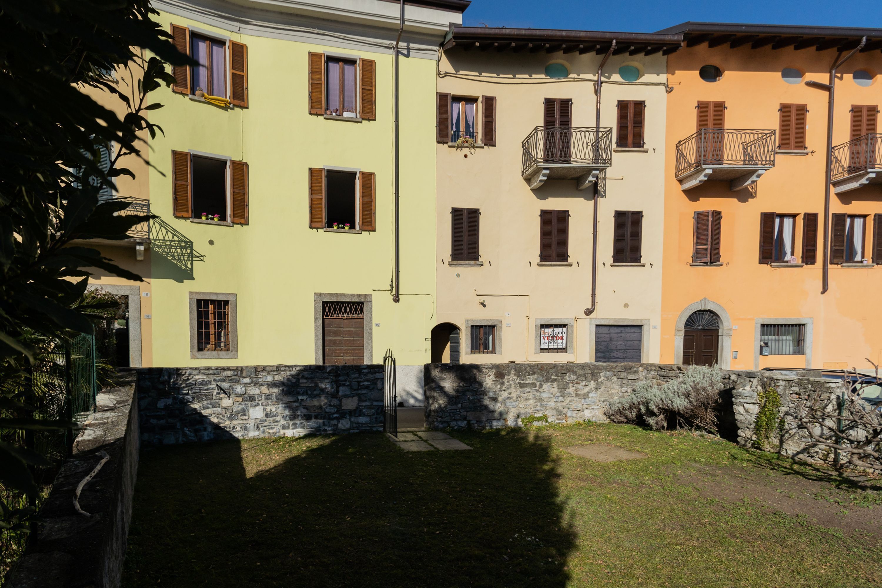 Una fila di edifici a più piani con balconi, un muro in pietra e un'area verde.