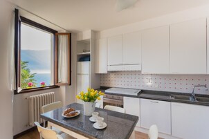 Una cucina moderna con mobili bianchi, un piano di lavoro in granito e vista sul mare attraverso una finestra.