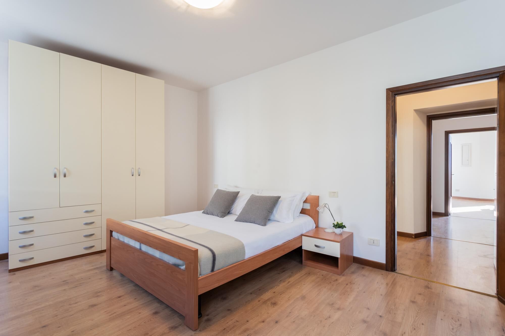 A bedroom with a wooden bed, a white wardrobe, and a nightstand with a lamp.