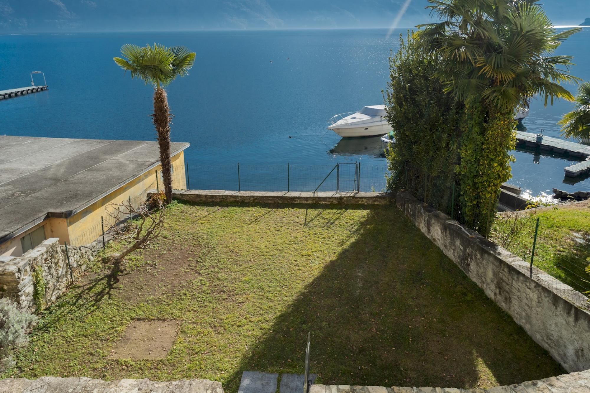 A view of a marina with a boat docked, a grassy area, and a building with a concrete roof.