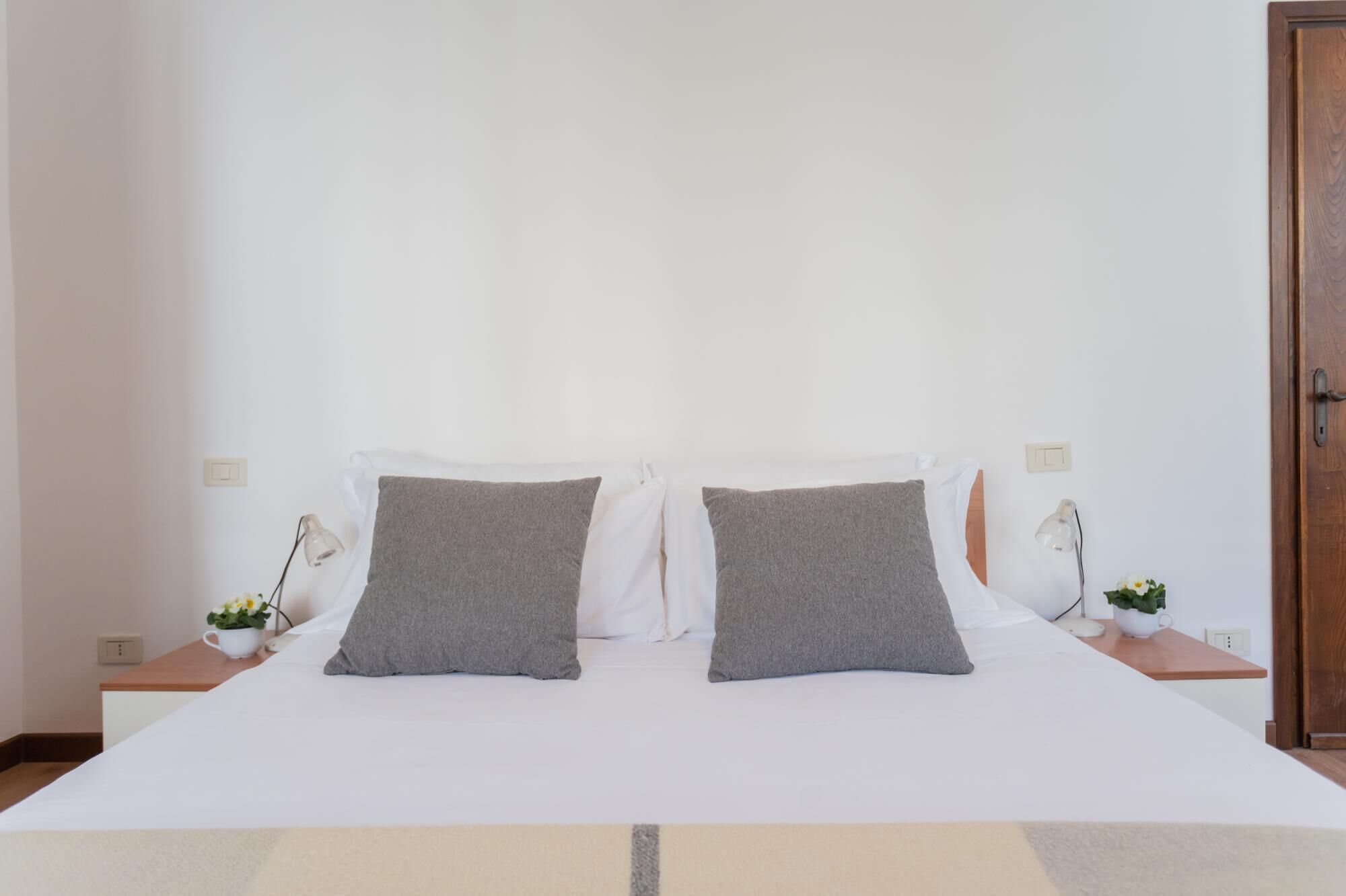 A neatly made bed with two pillows, a bedside table with a lamp, and a small potted plant.