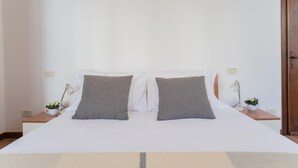 Ein ordentlich bezogenes Bett mit zwei Kissen, ein Nachttisch mit Lampe und ein kleiner Blumentopf.
