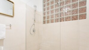 Eine Dusche mit Glastür, eine weiße Badewanne und eine geflieste Wand mit Marmoroptik.
