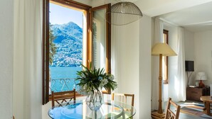 Ein Essbereich mit einem Glastisch, Stühlen, einer Vase mit Blumen, Blick auf einen Berg und das Meer sowie einer Lampe.