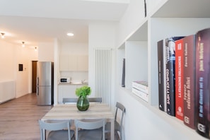 Une cuisine moderne équipée d’un four à micro-ondes encastré, d’un réfrigérateur en acier inoxydable et d’un coin repas avec une table et des chaises en bois.