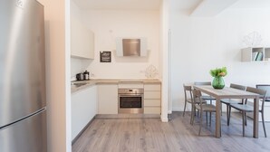 A modern kitchen with a built-in oven, a stainless steel refrigerator, and a dining area with a wooden table and chairs.