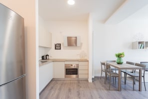 A modern kitchen with a built-in oven, a stainless steel refrigerator, and a dining area with a wooden table and chairs.