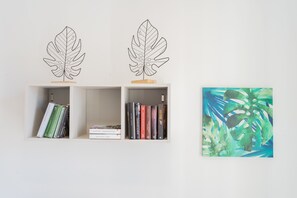 Deux décorations murales en forme de feuilles sont fixées au-dessus de deux étagères ouvertes, où sont rangés des livres.