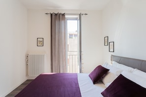 Une chambre avec un lit, un radiateur, une fenêtre avec des rideaux et une vue sur le balcon.