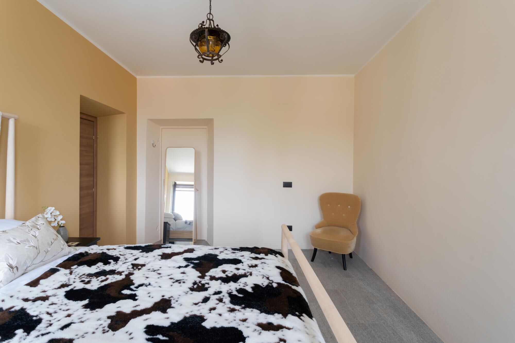 A bedroom with a bed, a chair, a door, and a hanging light fixture.
