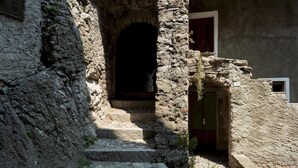 Un escalier en pierre mène à une porte en arc de cercle, avec une porte et une fenêtre visibles sur la droite.