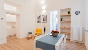 Ein modernes Wohnzimmer mit Esstisch, einem gelben Sessel, einem weißen Sofa und einer Küche im Hintergrund.