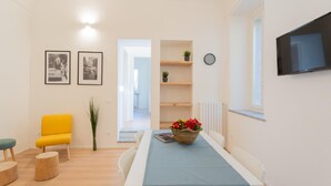 Ein modernes Zimmer mit Esstisch, einem gelben Sessel, einem Fernseher und gerahmten Bildern an der Wand.