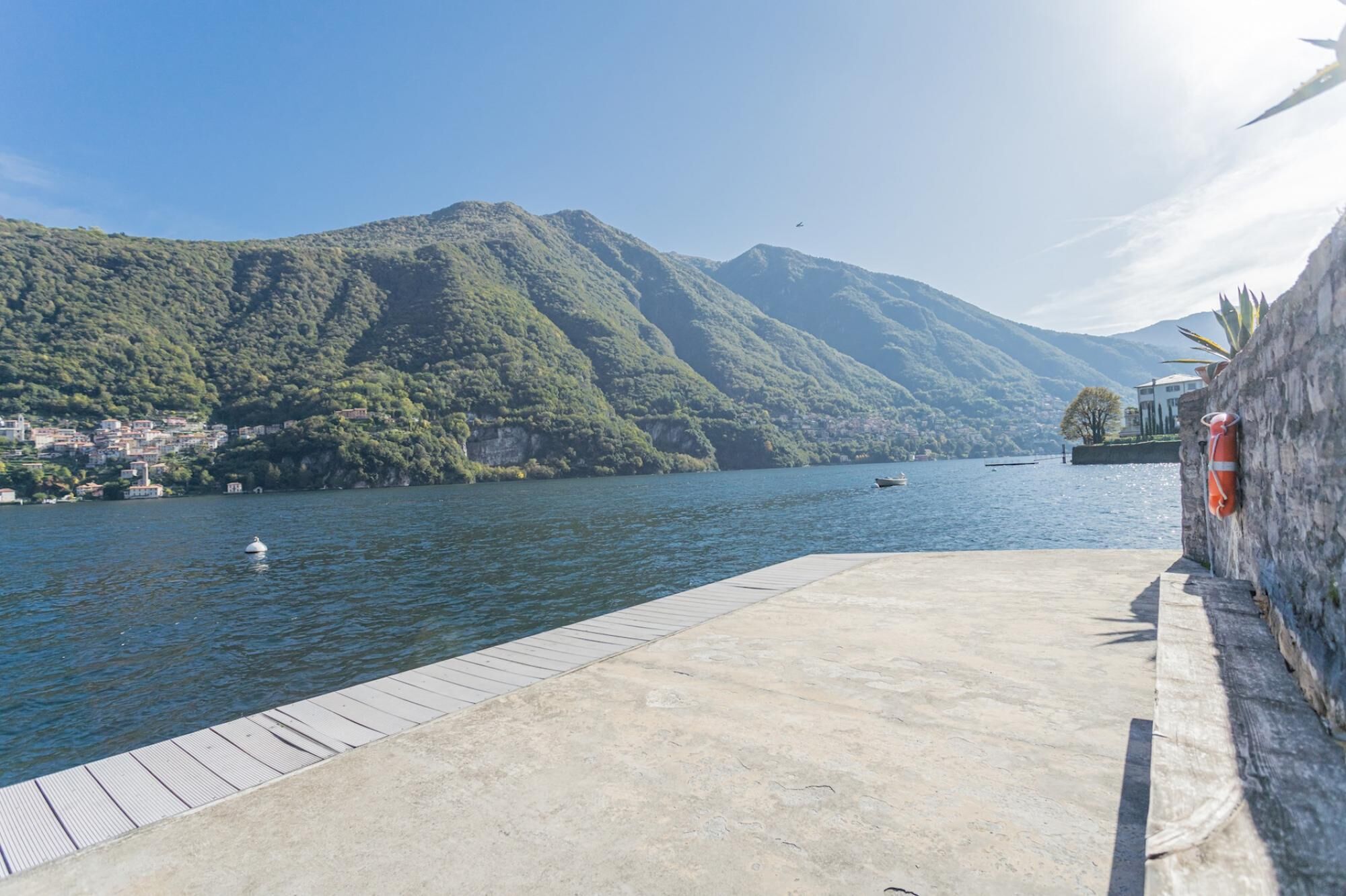 A waterfront dock with a concrete platform, a small boat, and a mountainous backdrop.