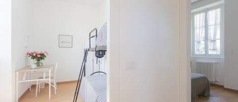 A bedroom with a bed, a desk with a chair, a radiator, and a window.