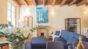 Un salon avec une cheminée, un canapé, une table ornée d’un vase de fleurs et un tableau accroché au mur.