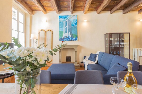 A living room with a fireplace, a sofa, a table with a vase of flowers, and a painting on the wall.