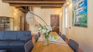 Un coin repas avec une table en bois, des chaises, un vase de fleurs et un escalier doté d’une rampe en métal.